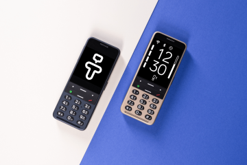 Two BlindShell feature phones on a split background of light beige and blue. The phone on the left is dark-colored and displays the Tandem app logo on its screen. The phone on the right is gold-colored, showing the time 12:30 and other status icons on its screen.