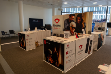 The BlindShell booth at SightCity 2026 in Frankfurt. The exhibition stand features large BlindShell Classic 3 branding, product displays, information panels, and demonstration devices. A large backdrop shows a family using BlindShell, while visitors can explore phone features such as Luna, Observo, and Tandem. The booth is arranged as a welcoming meeting space for product demonstrations and conversations with attendees.