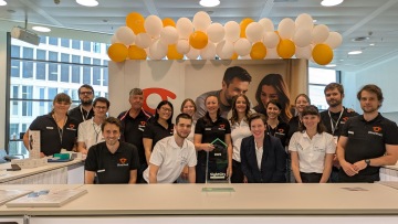 Foto de grupo del equipo BlindShell detrás de un stand en Sight City. Están sonrientes y reunidos en torno a un premio SightCity FeelVision. El stand está decorado con globos naranjas y blancos, y al fondo se ve una gran pancarta con caras amigas.