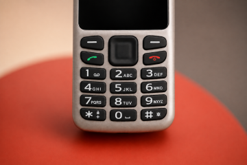 Close-up of the BlindShell Classic Lite keypad against a softly blurred warm beige, gray, and red background. The image highlights the large tactile number buttons.