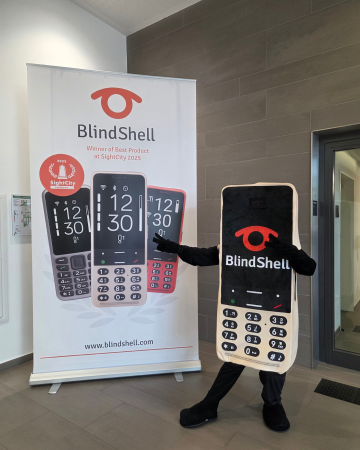 Our new BlindShell mascot, designed as a giant golden BlindShell phone with a keypad, screen, and bright BlindShell logo, poses proudly next to a BlindShell display banner. With its playful stance and friendly energy, the mascot quickly became a favorite among visitors, spreading smiles and bringing extra fun to SightCity 2026.