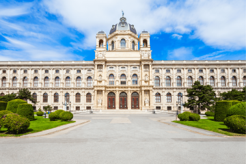 Vista frontal del Kunsthistorisches Museum en Viena, con una majestuosa cúpula, esculturas elaboradas y una fachada simétrica de estilo renacentista, rodeada de jardines bien cuidados.