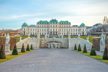 Un majestuoso palacio barroco con cúpulas de cobre verdes, arquitectura simétrica y estatuas ornamentadas en el jardín que conduce al edificio principal del Belvedere Superior en Viena, Austria.